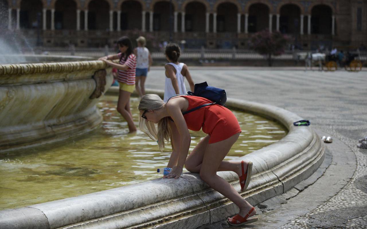 Een vrouw zoekt verkoeling bij een fontein op de Plaza de España in Sevilla, Spanje. 
