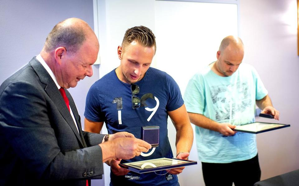 Sido van der Meulen en Martin Feringa bekijken de onderscheiding van burgemeester Tom van Mourik.