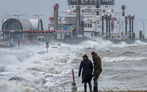 Enkele mensen kijken hoe de door de storm opgezweepte golven over de veerdam van Ameland gaan.