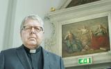 Pastoor Paul Verheijen op foto bij schilderij geloof, hoop en liefde in de Grote Kerk van Dokkum.