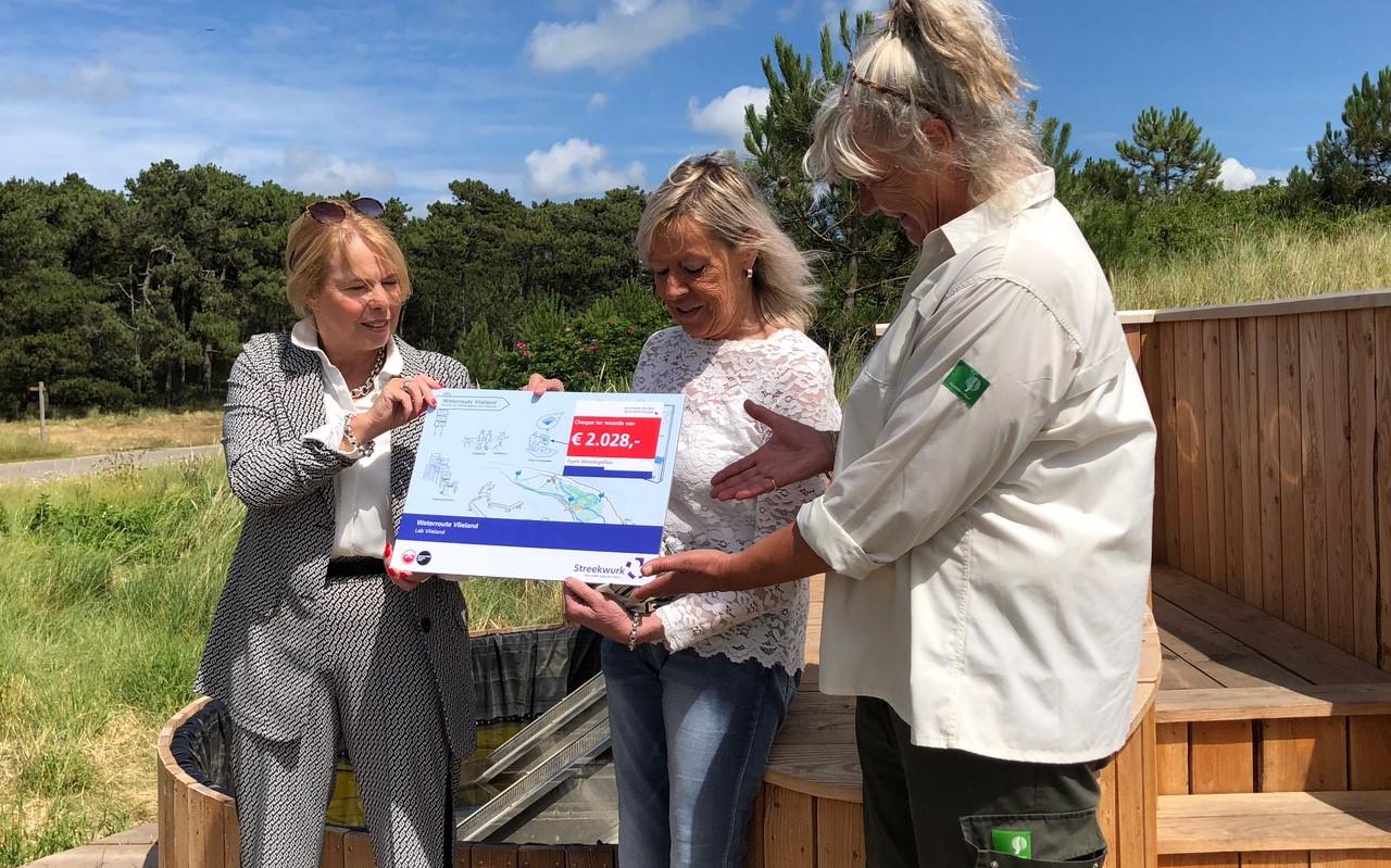Gedeputeerde Avine Fokkens (links) overhandigt de cheque van 2028 euro aan Annie Beiboer van VVV Vlieland en Anke Bruin-Kommerij van Staatsbosbeheer.