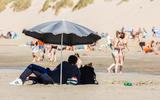 Badgasten blijven in de schaduw onder parasol op het strand van Hollum, Ameland (13 augustus).