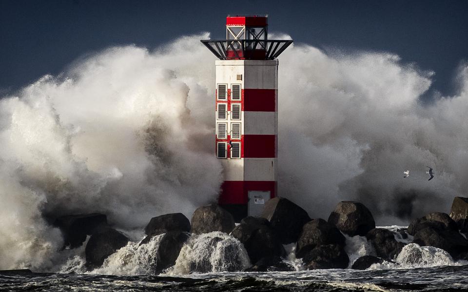 Grote golven slaan tegen het baken op de kop van de pier van IJmuiden tijdens een storm.