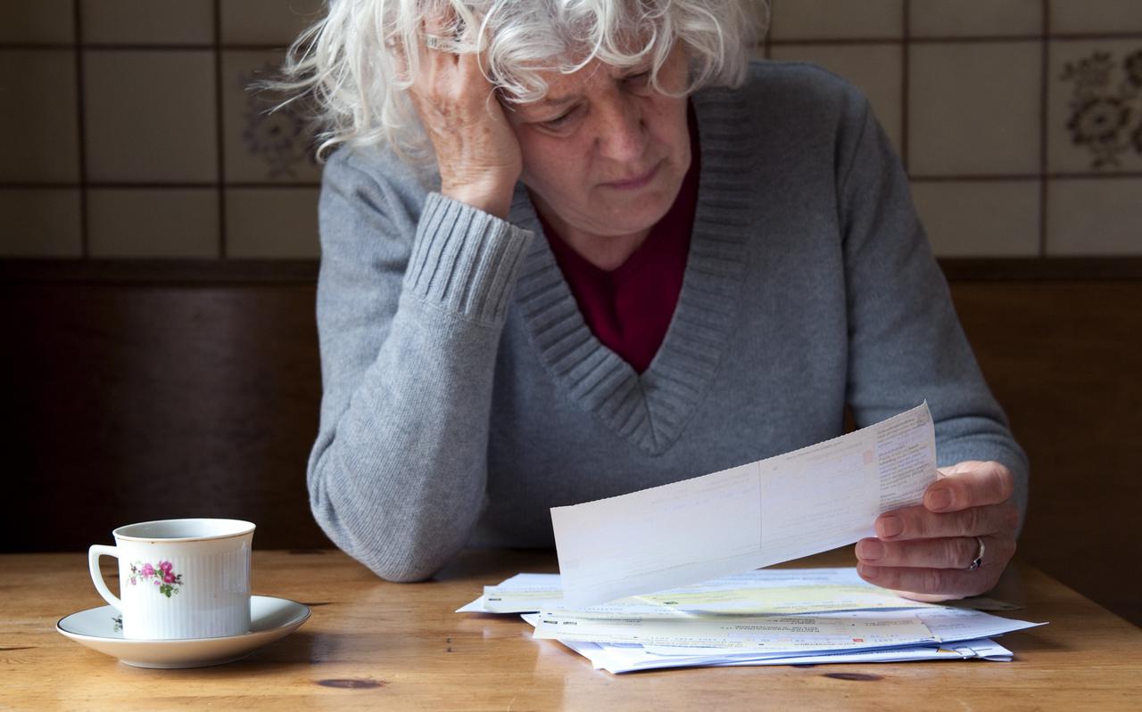 Een gepensioneerde dame bekijkt een stapel rekeningen.