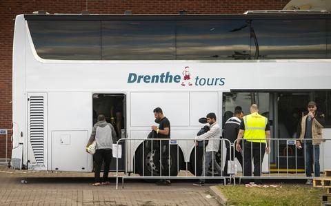 Asielzoekers stappen in een bus die binnen de hekken van het aanmeldcentrum van Ter Apel staat.