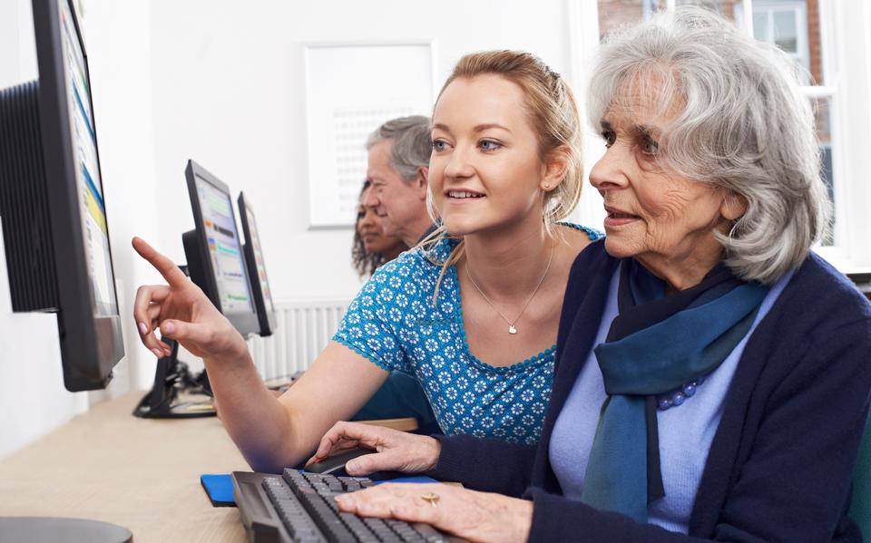 Een oudere vrouw krijgt advies bij het invullen van een digitaal formulier.