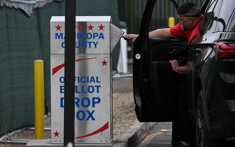 Een chauffeur laat een stembiljet achter in een stembus bedoeld voor vroege verkiezingen in Arizona. 