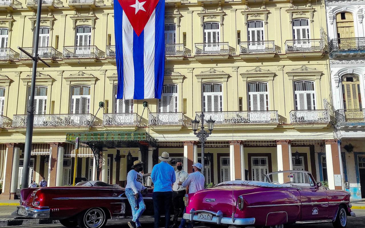Bestuurders van oude Amerikaanse auto's praten vlakbij een Cubaanse vlag bij het Inglaterra Hotel in Havana. 