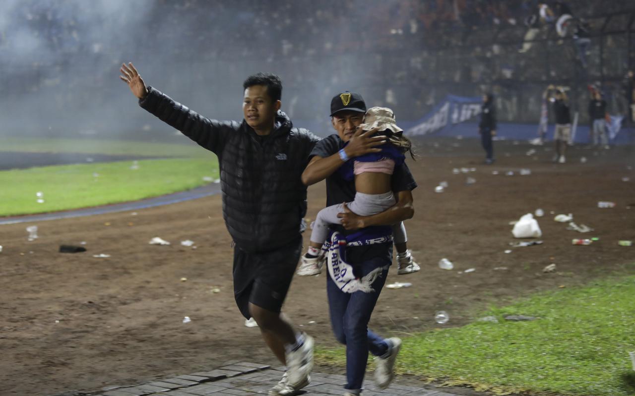 Voetbalsupporters brengen een meisje in veiligheid tijdens de rellen in het stadion van Malang. 