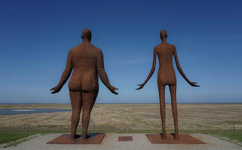 De twee beelden van het kunstwerk 'Wachten op hoog water' kijken vanaf de Waddendijk bij Holwert uit over het kwelderlandschap. 