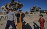 Afghaanse kinderen spelen naast vernietigde Amerikaanse wapens. De taliban hebben het wapentuig neergezet om hun overwinning in 2021 te vieren. 