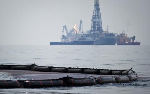 Gelekte olie wordt opgevangen op zee, met op de achtergrond de plek van het gezonken platform Deepwater Horizon in de Golf van Mexico in 2010. 