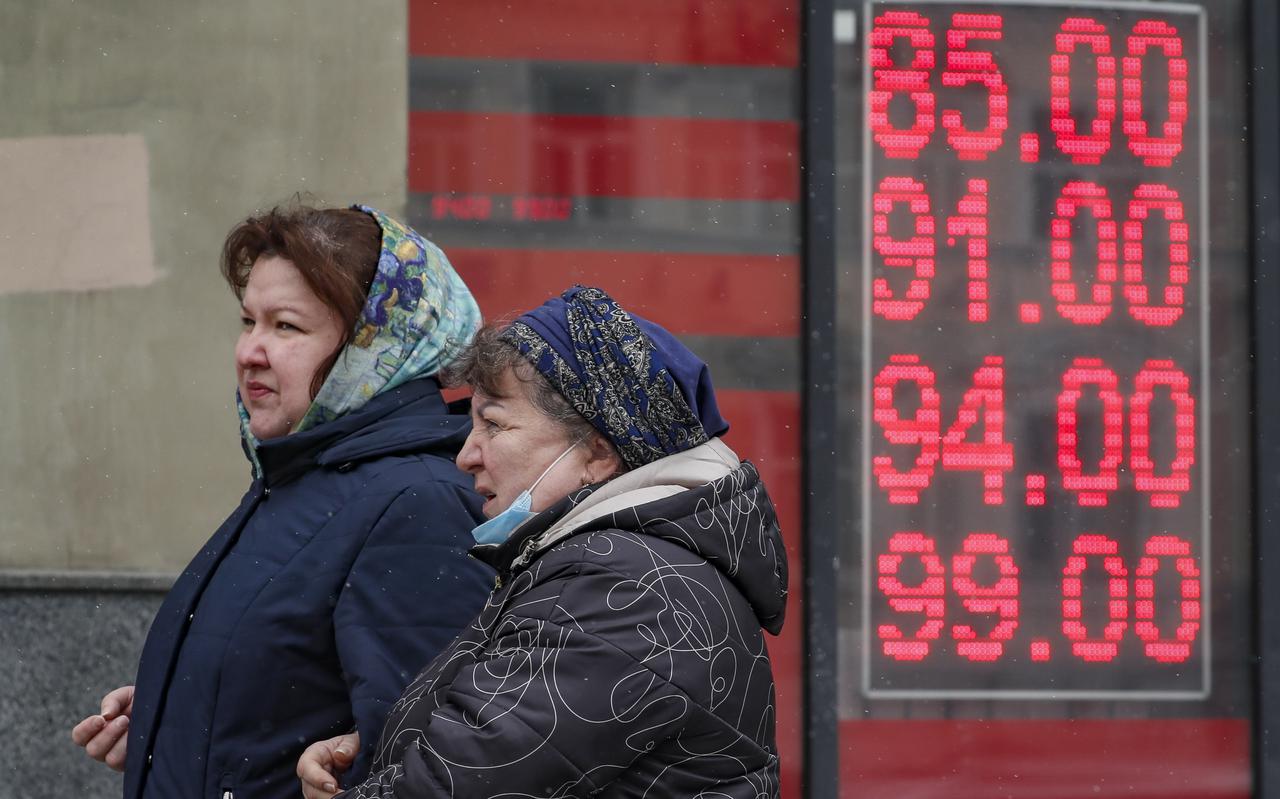 Vrouwen in Moskou lopen langs een bord met wisselkoersen van de roebel.
