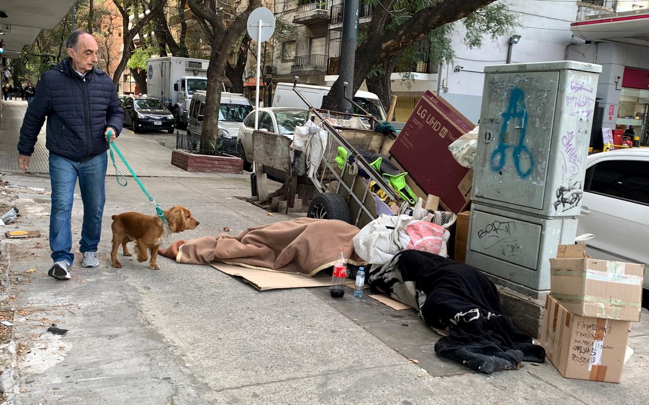 Een man loopt met zijn hond langs twee slapende daklozen op een trottoir in Buenos Aires. Een man loopt met zijn hond langs twee slapende daklozen op een trottoir in Buenos Aires.