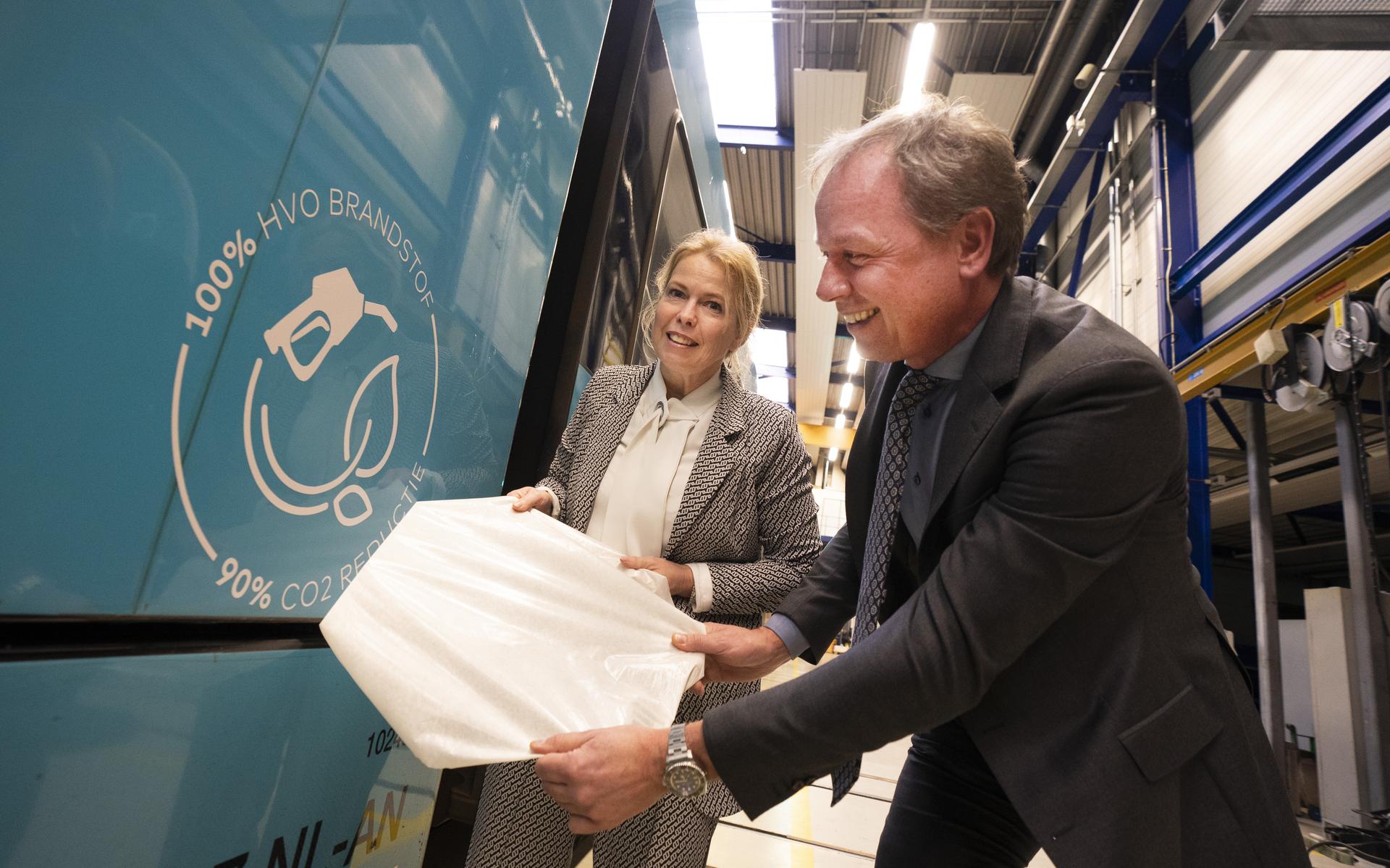 Milfred Hart, regiodirecteur Noord van Arriva, en Avine Fokkens-Kelder, gedeputeerde Verkeer en Vervoer van de provincie Fryslân plakken een HVO-sticker op een trein van de vervoerder.