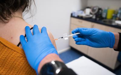 Een huisarts vaccineert een patiënt in zijn praktijk. 