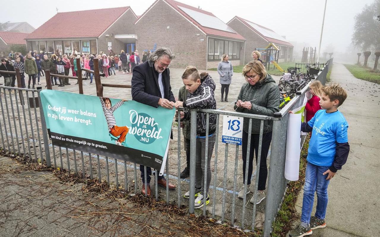 Roel de Jong, wethouder van de gemeente De Fryske Marren hangt samen met leerlingen van De Trieme een banner aan het hek van de school.