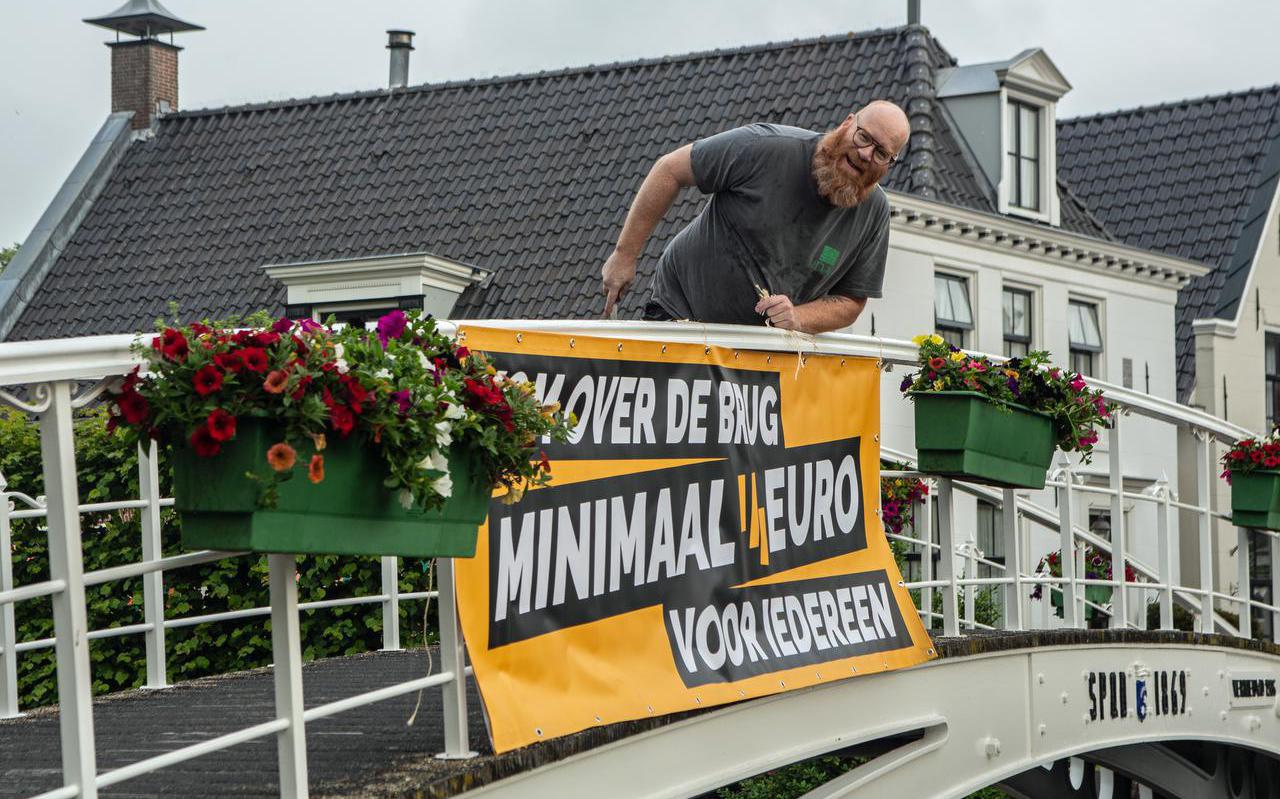 Wouter Pieterse hangt in juni 2021 een spandoek op de Turfmarktbrug in Dokkum. Het vormt het begin van de actie van de FNV voor een hoger minimumloon voor iedereen. 
